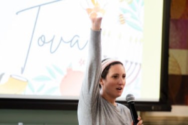A person standing in front of a display of the word Tova with their arm extended and hand open