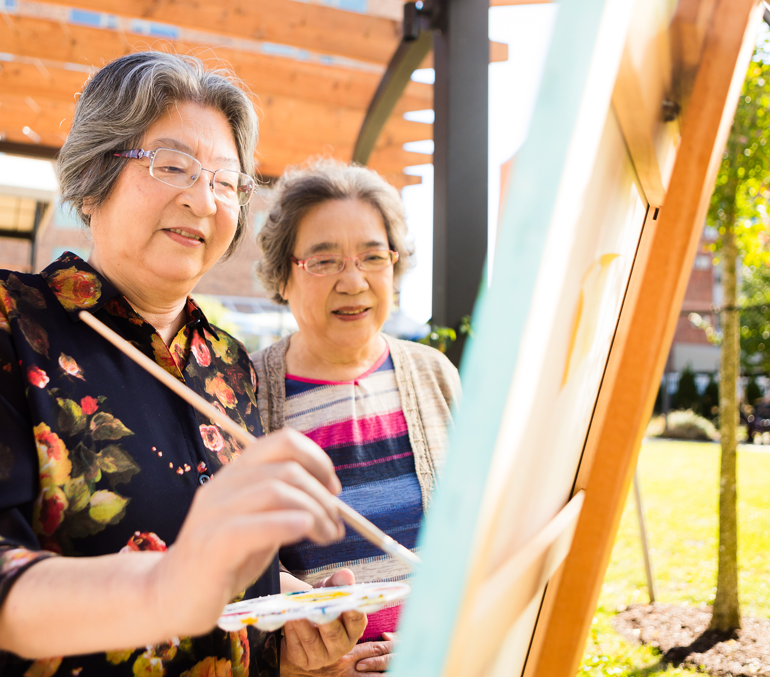 Two women painting together outdoors on the Brighton campus.
