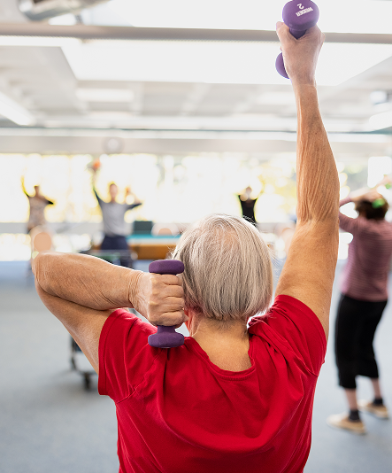 A senior woman lifting hand weights in a group exercise class.
