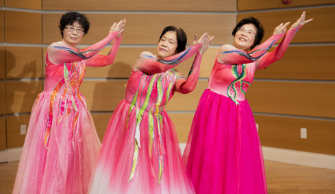 3 Asian women dancing in pink dresses with ribbon trim