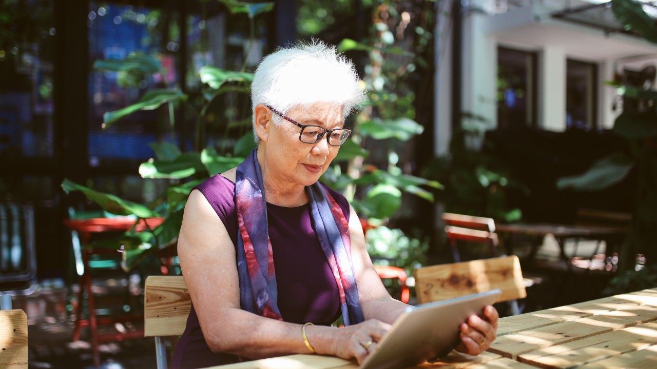 A woman outside sitting at a table using a tablet