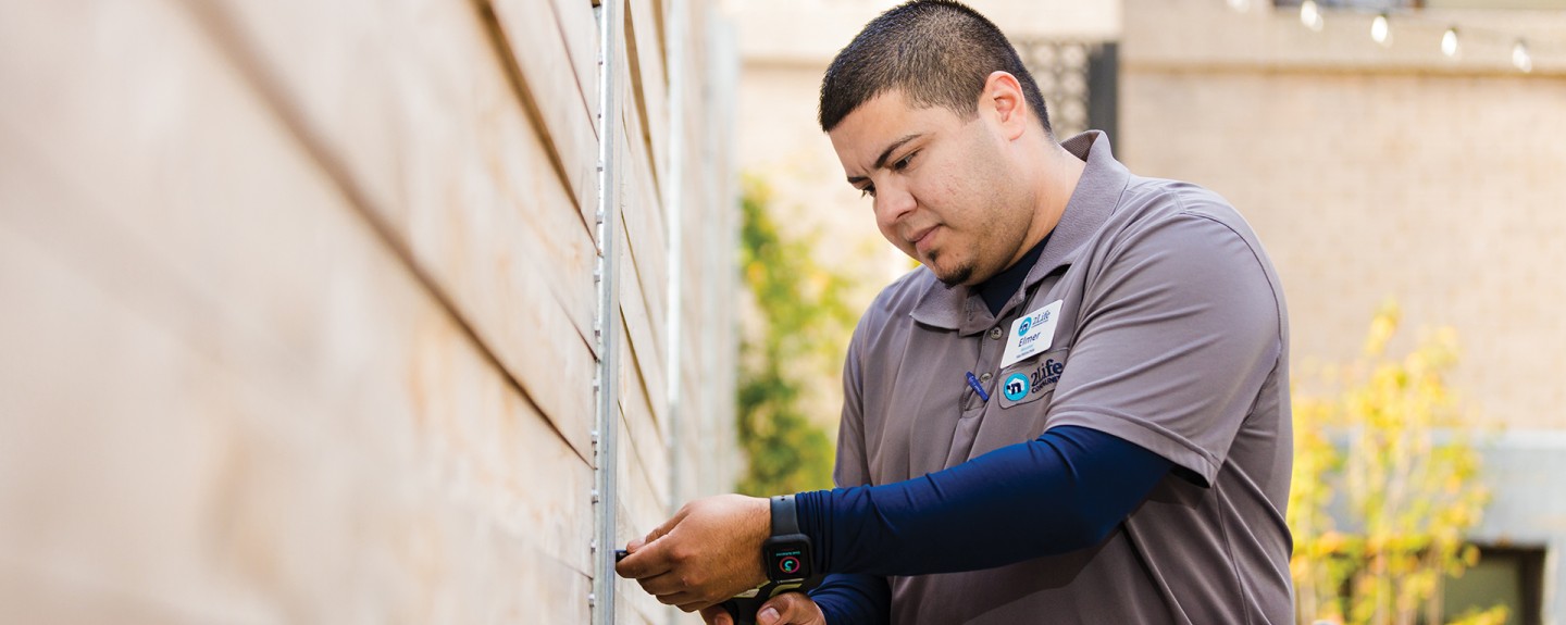 A uniformed medium toned person uses a drill on the side of a building