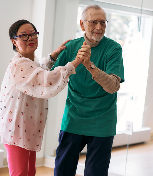 Two seniors dancing together and smiling in a bright room.
