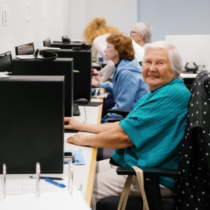 Seniors using computers in a classroom setting, one smiling at the camera.