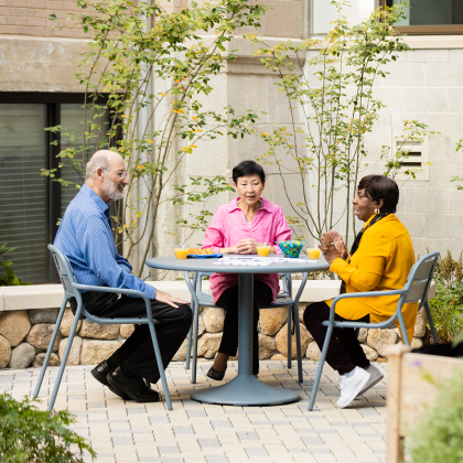 Three seniors sitting at an outdoor table, talking and enjoying refreshments.