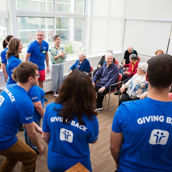 A group in a room, some standing in blue shirts, some seated