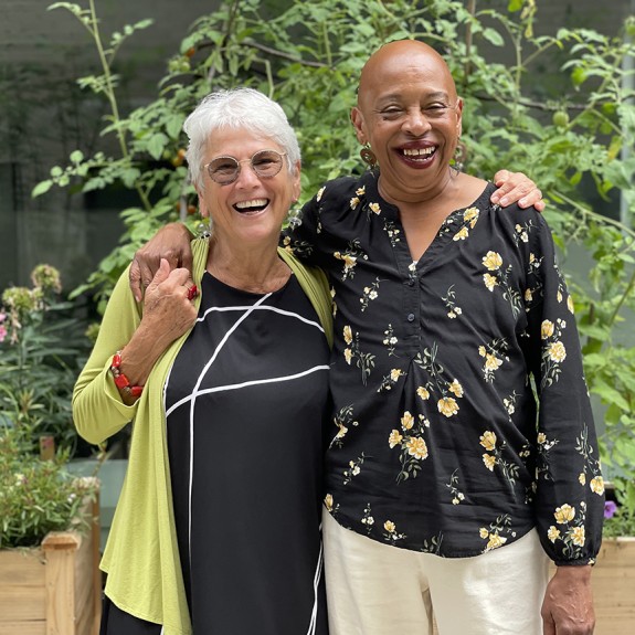 Two women standing in a garden with arms around each other's shoulders