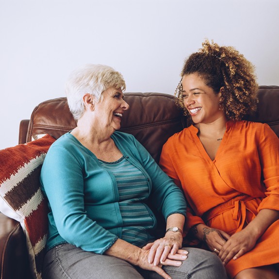 Two women sitting side by side on a couch with their hands folded.