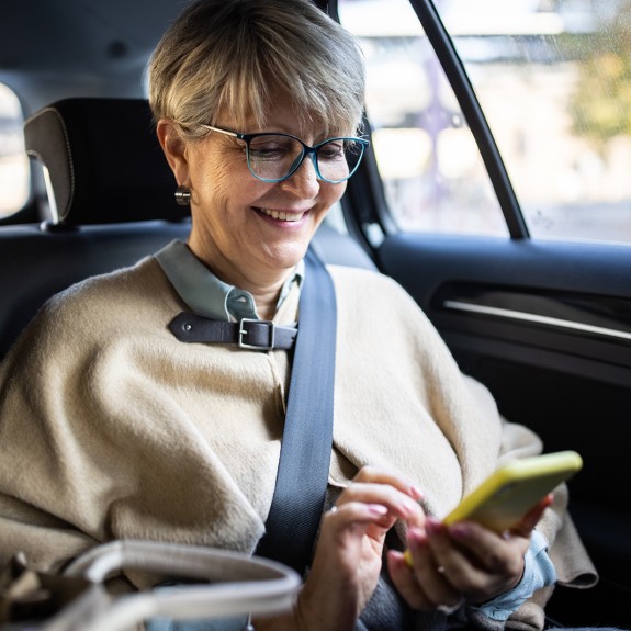 A woman smiles at her phone in the back seat of a car