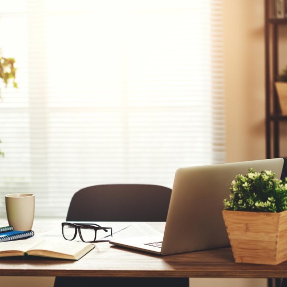 An office with an opened laptop, a plant, and glasses on the desk