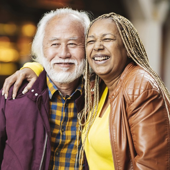 Two people standing, one with their arm around the other's shoulders, both smiling