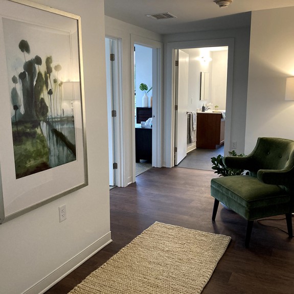 A room with a chair, a lamp, a white floor runner, and a piece of art on the left wall