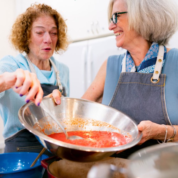 A person holds red soup in a bowl as another person stirs