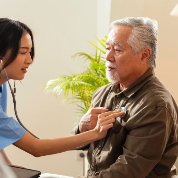 An Asian health professional holds a stethoscope to the chest of an older Asian man
