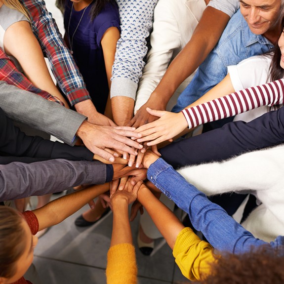 A group of people huddle and pile their hands