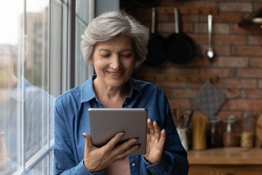 A woman sitting next to a window scrolling a tablet