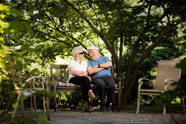 Two people sitting together on a bench outside among trees