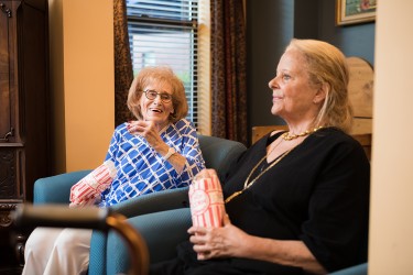 Two women seated in chairs; one is eating popcorn