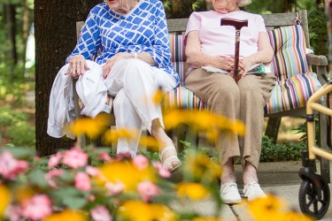 Two women sitting outside on a bench with flowers in the foreground