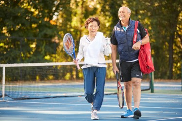 Two people walking off the tennis court together carrying equipment