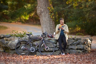 A woman leaning against a stone wall next to a bicycle