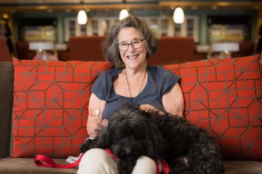 A person sitting on a couch against a red pillow with a dog in their lap