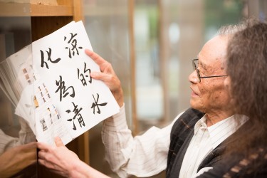 A person opens an Asian language book on a shelf while another looks on