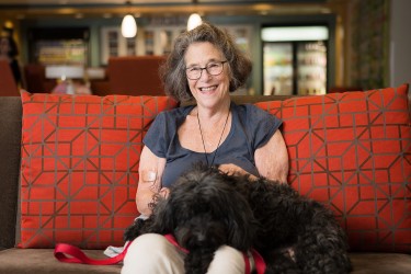 A person sitting on a couch against a red pillow with a dog in their lap