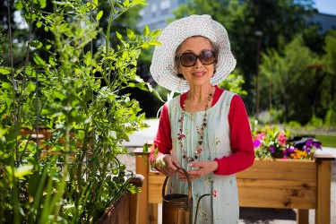 A person wearing a white hat, white dress, red shirt, and sunglasses working in a garden