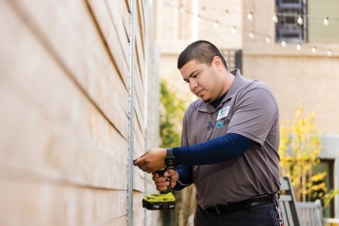 A uniformed medium toned person uses a drill on the side of a building