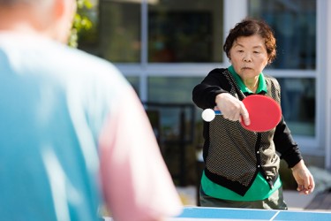 An Asian woman holds a paddle while playing ping pong