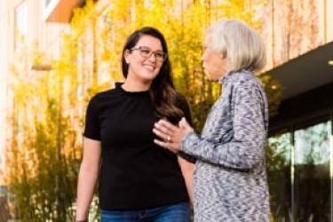 A younger light toned person wearing black talking outside to an older person wearing a white patterned shirt