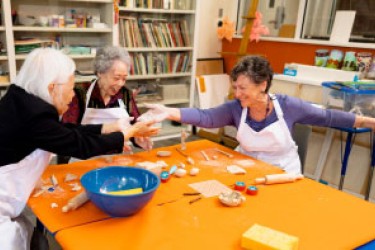 Three people extending hands over craft supplies on a table