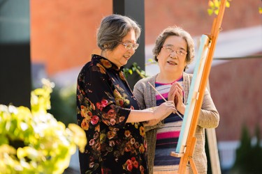 One person painting outside as another stands nearby