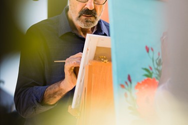 A man with a goatee and glasses painting a picture
