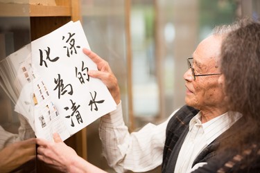 An Asian person holds open a large print book on a shelf
