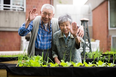 Two Asian people waving in front of a garden bed