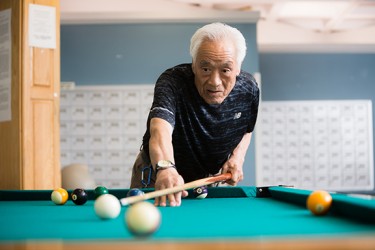 An Asian man playing pool on a pool table