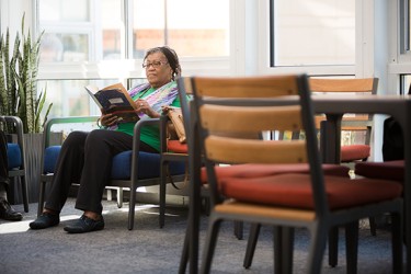 A person reads a book in a sunny room surrounded by chairs