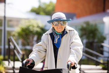 A person in a gray hat, glasses and white jacket pushing a wheelchair