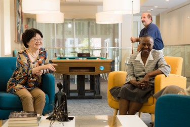 Two people sitting in a rec room as a person stands behind them